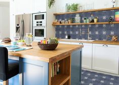 a kitchen with blue and white tiles on the wall, wooden counter tops and chairs