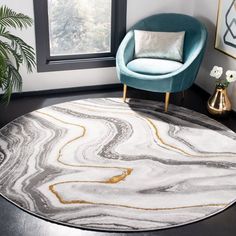 a round rug with an abstract design in grey and gold on the floor next to a blue chair