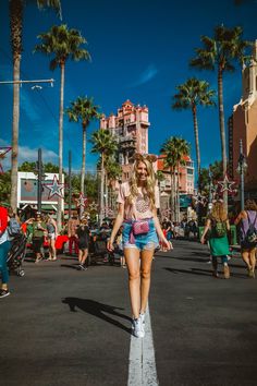 a woman is walking down the street in front of some palm trees and other people