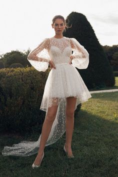 a woman standing in the grass wearing a white dress with sheer sleeves and high heels