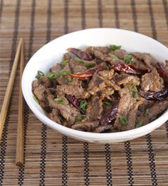 a white bowl filled with meat and vegetables next to chopsticks