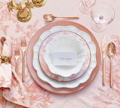 a place setting with pink and white plates, silverware, napkins and gold cutlery