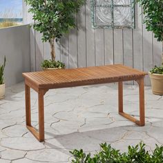 a wooden table sitting on top of a patio next to potted plants and trees