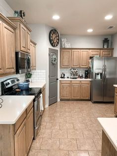 a kitchen with stainless steel appliances and wooden cabinets is shown in this image, there are two clocks on the wall above the stove