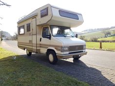 an rv is parked on the side of the road in front of a grassy field