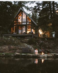 two people sitting on rocks in front of a house at night with the lights on