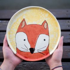 a hand holding a plate with a painting of a fox on it's face