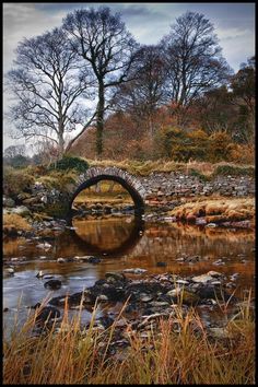 a stone bridge over a small stream in the middle of a field with trees and rocks