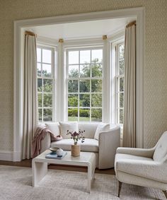 a living room filled with white furniture and large windows covered in drapes, along with a rug on the floor