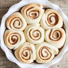 a white dish filled with cinnamon rolls on top of a wooden table