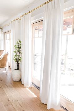 a living room filled with furniture and white drapes on the windowsill, next to a potted plant