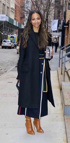 a woman in black coat and boots standing on sidewalk