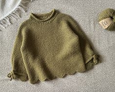 a green sweater sitting on top of a bed next to a ball of yarn