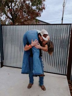 two people hugging each other in front of a fence