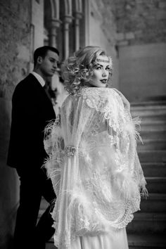 black and white photograph of a woman in a dress with feathers on it, standing next to a man wearing a tuxedo