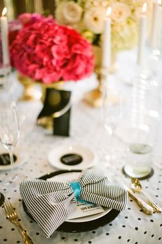 the table is set with black and white plates, silverware, and pink flowers