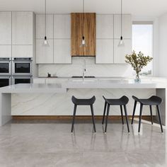 a kitchen with marble counter tops and two stools in front of an island that's surrounded by white cabinets