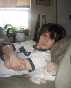 a young man laying on top of a couch holding a white and orange cat in his lap