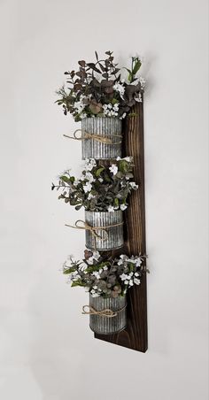 three metal buckets filled with flowers hanging from a wooden rack on a white wall