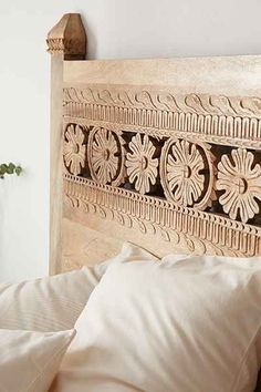 a wooden headboard with decorative carvings on it's sides and two pillows in the foreground