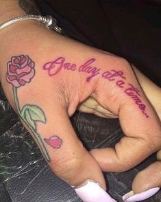 a person with a rose tattoo on their left hand and the words, one day at a time written in pink ink