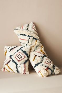 two decorative pillows sitting on top of a white shelf next to each other in front of a beige wall