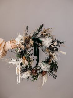 a wreath with white flowers and greenery hanging from the ceiling in front of a gray wall