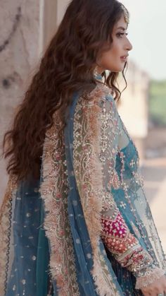 a woman in a blue and white outfit with long hair standing on the street, looking off