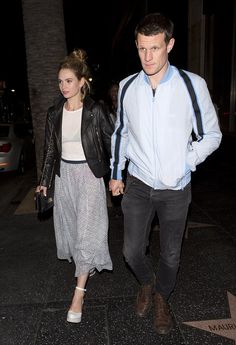 a man and woman are walking down the street holding hands while dressed in casual clothing