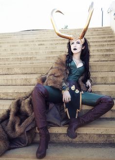 a woman with horns sitting on the steps in front of some stairs wearing green and brown