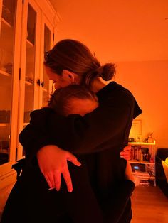 a woman holding a baby in her arms while standing next to a wall with orange light