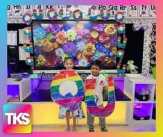 two young children holding up kites in front of a tv screen with the caption's name on it