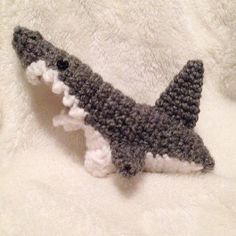 a crocheted stuffed shark laying on top of a white bed sheet with its mouth open