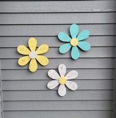 three wooden flowers are painted yellow, blue and white on the side of a house