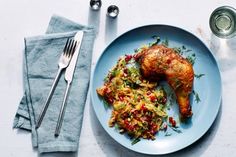 a blue plate topped with chicken and vegetables next to silverware on a white table