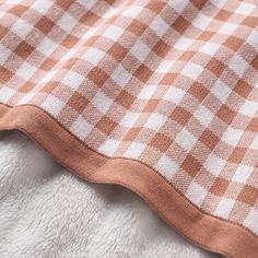 an orange and white checkered blanket laying on top of a tablecloth with brown trim