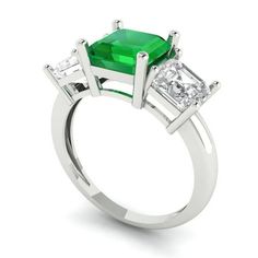 an emerald and diamond three stone ring with two princess cut diamonds on each side, set in white gold