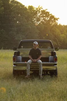 a man sitting on the back of a pick up truck in a field with trees