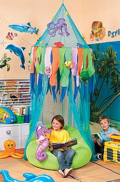 two children sitting on bean bag chairs in front of a play tent with octopus decorations