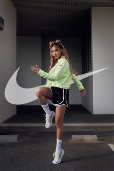 a woman in yellow jacket and black shorts posing for the camera with her nike shoe