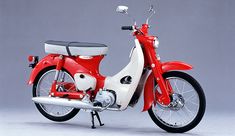 a red and white motor scooter parked on top of a gray floor next to a wall