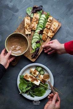 two hands holding chopsticks over a plate of food with cucumbers and sauce