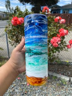 a hand holding up a glass with an ocean scene painted on the outside and inside