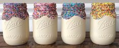 three mason jars filled with sprinkles on top of a wooden table next to a wall