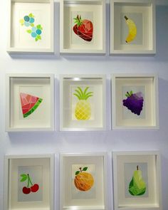 the wall is decorated with many different fruits and vegetables in white frames, all hanging up against a purple wall