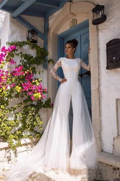 a woman standing in front of a blue door wearing a white wedding dress with sheer sleeves