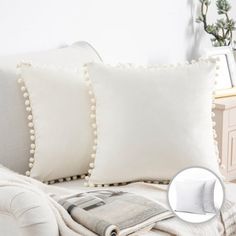 two white pillows sitting on top of a couch next to a pillow with pom - poms