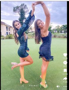 two young women in short dresses are dancing on the grass with their arms up and legs spread out