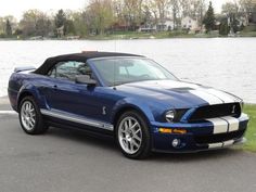 a blue mustang parked in front of a body of water