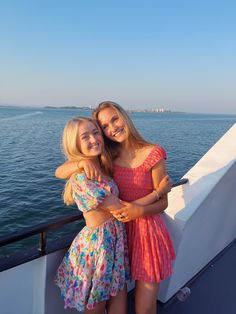 two girls hugging each other on the back of a boat in the ocean with blue sky and water behind them